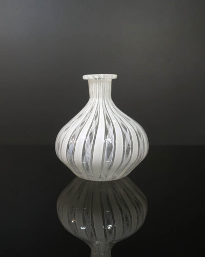 Stout shaped mouth-blown vase with finely rolled opening. About 4 inches tall. Fine white Latticino cane fillagree designs run vertically. There are occasional small bubbles, a result of the handmade glassblowing process called "Zanfirico". Similar designs were produced by Venini from Murano, Italy.